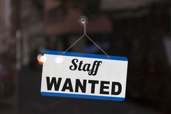 Close-up on a blue open sign in the window of a shop displaying the message: Staff wanted.