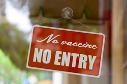 Close-up on a red sign in the window of a shop displaying the message: No vaccine, no entry .
