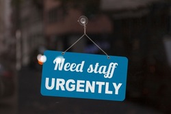 Close-up on a red and white sign in a window with written the message - Need staff urgently -.
