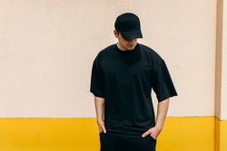 Man wearing black blank t-shirt and a black baseball cap with space for your logo or design. Mock up