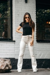 Stylish brunette girl wearing black t-shirt and white flared pants posing against street , urban clothing style. Street photography
