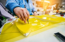 Applying colored yellow membrane to a surface of plastic 3d letter of signboard. worker's hands close up	
