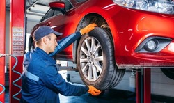 Expert specialist technician changes tires, tyres of lifted up car at auto service, wears uniform costume.