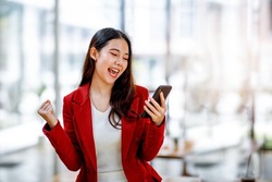 Excited happy woman looking at the phone screen, celebrating an online win, overjoyed young asian female screaming with joy, isolated over a white blur background