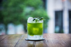 you can see a cocktail called gin basil smash standing on a table whose green color is strong and has a blurry background