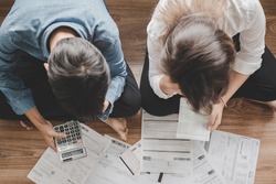 Top view asian couple sitting on the floor stressed and confused by calculate expense from invoice or bill, have no money to pay think of taking the house to mortgage causing debt, bankruptcy concept.