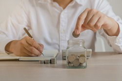 Close up hand of young asian businessman,male puts a coin into the jar to calculate and financial plans to spend enough money on his income for saving money and payment, payday.Finance people concept.