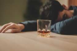 Alcoholism, depressed asian young man sleep on table while drinking alcoholic beverage, holding glass of whiskey alone at night. Treatment of alcohol addiction, suffer abuse problem alcoholism concept