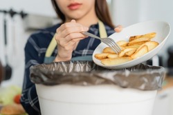 Cholesterol of junk meal is fat meal, hand of asian young household woman scraping, throwing food leftovers into garbage, trash bin from potato chip, snack. Environmentally responsible, ecology