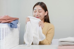 Feel softness, smiling asian young woman, girl touching fluffy towel cotton, smelling fresh clean clothes on table after washing, laundry, dry. Household working at home. Laundry and maid.