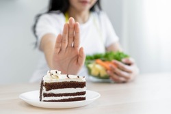 Diet, Dieting asian young woman using hand push out, deny chocolate cake or sweet taste, dessert food, choose eat green salad vegetables when hungry. Nutritionist of healthy, nutrition of weight loss.