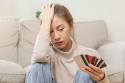 Financial owe asian young woman, girl sitting suffer, stressed and confused, sitting and holding many credit card, no money to pay expense, mortgage or loan. Debt, bankruptcy or bankruptcy concept.