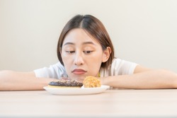 Diet, dieting asian young woman, girl expression face bored, looking at doughnut, bakery and fried chicken, fast food in plate to loss weight. Passion, temptation when hungry restrained to eat.