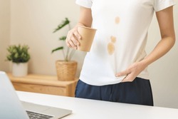 Cloth stain, disappointment asian young woman clumsy with hot coffee, tea stains on shirt, hand show making spill drop on white t-shirt, spot dirty or smudge on clothes at home, isolated on background