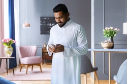 Saudi man standing in living room at home using phone