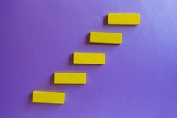 Wooden blocks arranged in the form of stairs. Top view of yellow blocks isolated on purple background. Business concept for growth, process, success.