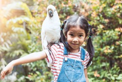 Cute asian child girl with beautiful macaw parrot in her shoulder in the zoo