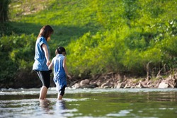 Asian mother holding her child hand to walk and play in the river together with fun and enjoy with nature.