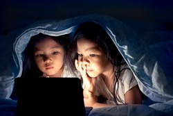 Two asian little girls using digital tablet under blanket at night in dark blue color tone