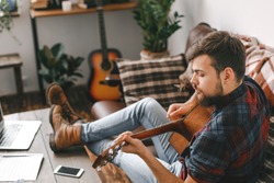 Young guitarist hipster at home playing guitar concentrated