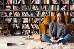 Young woman writer in library at home creative occupation sitting writing notes