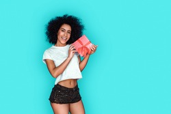 Young mixed race girl standing isolated on blue wall holding present box posing camera smiling playful