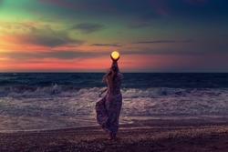The girl holds the moon in her hands. Beautiful sunset on the sea. Dreams come true. Everything is possible.