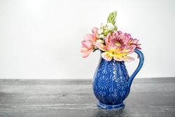 Small blue ceramic vase filled with two pink dahlia flowers and a variety of freshly cut flowers from a garden. White background and weather black wood base.