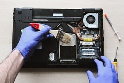 disassembled laptop. repair and maintenance of laptops. removing dust with a brush. hands in the frame