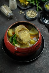 Selective focus of Sup Kikil (beef tendon soup) - Shiny, Oily and Fatty of Indonesian beef tendon soup with vegetables served in red bowl over dark textured backdrop with ingredients
