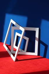 Still life: white square and rectangular frames with shadows on a blue and red background with a wooden texture. Abstract art design composition