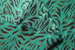 Decorative background texture: green silk pleated fabric. Turquoise tissue with bird feathers, dress textile with folds. Chiffon cloth, wild exotic tropical pattern with black tiger stripes