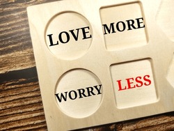 Text LOVE MORE WORRY LESS writing on wooden board on wooden background.