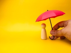 Hand holding red umbrella with peg doll on a yellow background.Insurance cover concept.