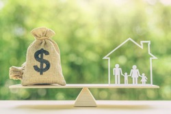 Cost of living, home loan, family finance and child trust fund concept : US dollar bags, family members live inside a house on basic balance scale, depicts the expenditure a family should prepare for