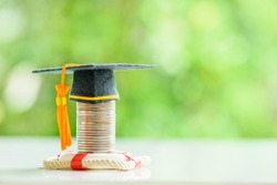 Tuition protection service and tuition refund insurance, financial concept : Black graduation cap or a mortarboard placed higher on top of a coin stack with a red lifebuoy on a table, green background