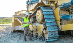 maintenance manager taking notes on an inspection of a heavy road making machine, bulldozer, large construction tractor