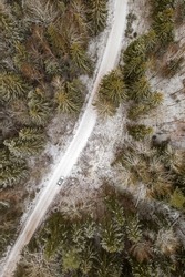 Car on rural road in winter with snow covered trees aerial view