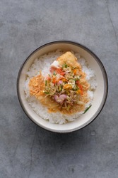 A dish of Rice Bowl, with Crispy Fried Dory Fish, with sliced garlic, shallot, chili, oranges leaves as Sambal Matah on it.
