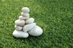 Close up Stack of white pebble stones, Arranged in the shape of a pyramid, on the artificial green grass, Concept of simplicity and Asian spirit, with space for your text