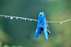 An image of blue cloths pin or peg on a clothesline on rainy day countryside of India.Close up of colorful plastic laundry latch.selective focus with nice creamy blurry background.