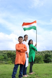 3 Indian students  or children holding or waving Tricolour with greenery in the background, celebrating Independence or Republic day