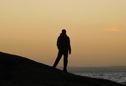silhouette of a person standing on the rocks watching the sunset over the lake