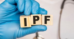 IPF Idiopathic pulmonary fibrosis - word from wooden blocks with letters holding by a doctor's hands in medical protective gloves. Medical concept.