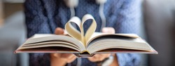 Book lover or love reading concepts. Male hand holding book with heart shape page folded.
