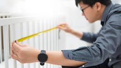 Asian man using tape measure for measuring dimension of toddler bed rails length and gap. Choosing furniture for kids or children in the house at furniture store.