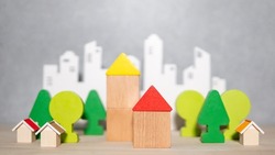 Group of wooden house and tree toy block models with blurred city background on the table. Urban living concept