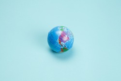 an antistress ball representing the planet earth, isolated on a plain turquoise background. Minimal still life color photography.
