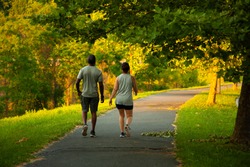 Image of an African American man and a caucasian woman walking on a hiking trail. The couple wears matching vests, shirts, shorts and sneakers. These two people walk peacefully on a sunny day