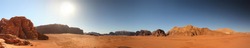 A panoramic view of the spectacular Wadi Rum desert in Jordan featuring unique red sandstone cliffs, mountains and a large desert plain on the foothills of these rock formations. 